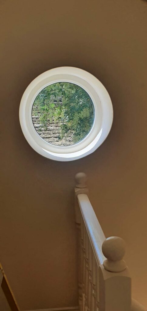 Fully round white timber look windows bringing light into a stairwell